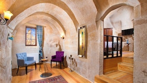 Une pièce avec un plancher en bois, deux chaises, un tapis, un chandelier et un escalier.
