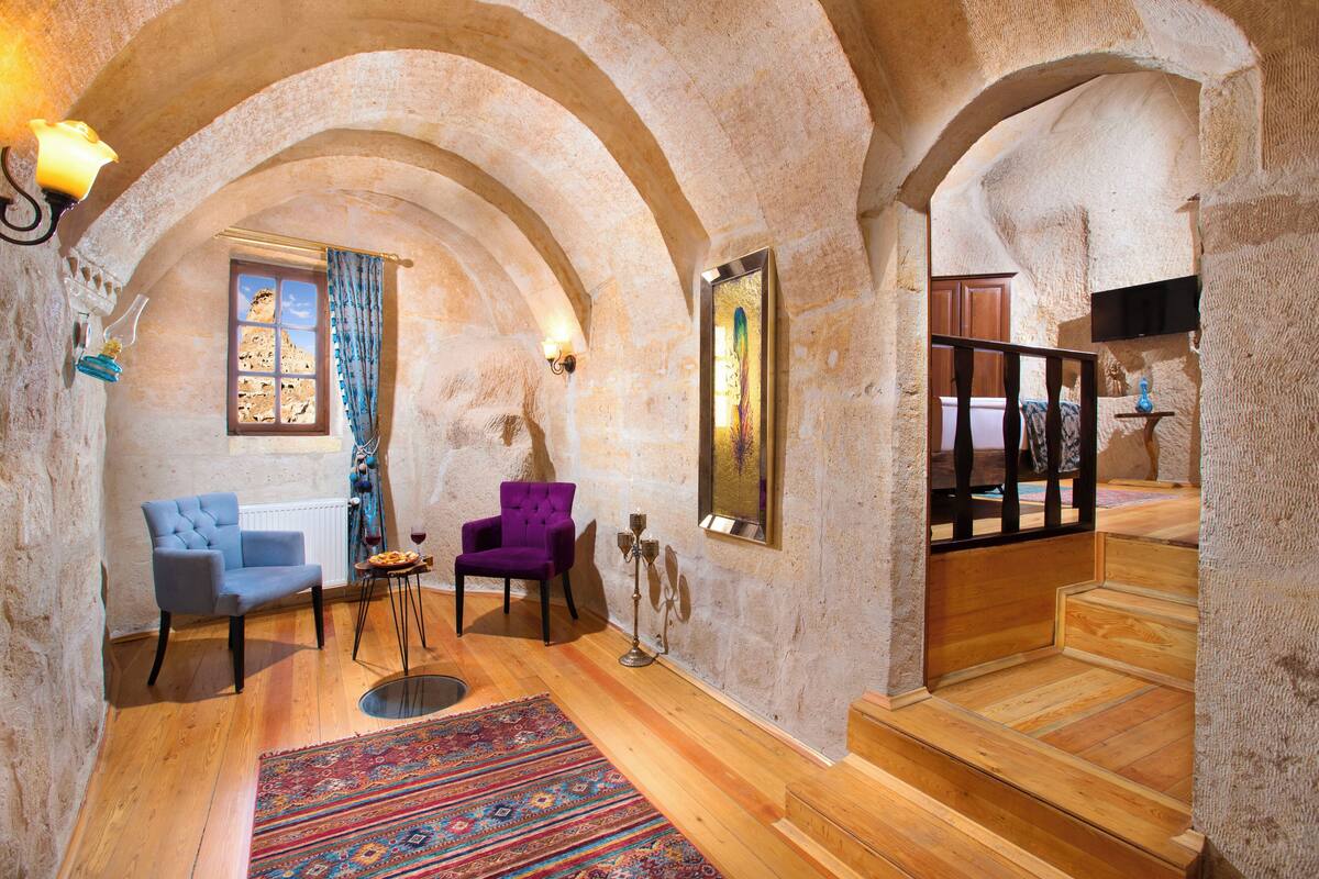 A room with a wooden floor, two chairs, a rug, a candelabra, and a staircase.