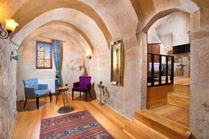 Una habitación con piso de madera, dos sillas, un tapete, un candelabro y una escalera.