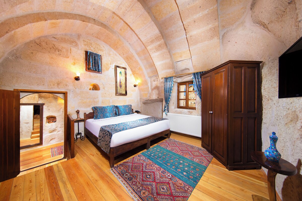 A bedroom with a wooden bed, a large rug, a wardrobe, and a stone wall.