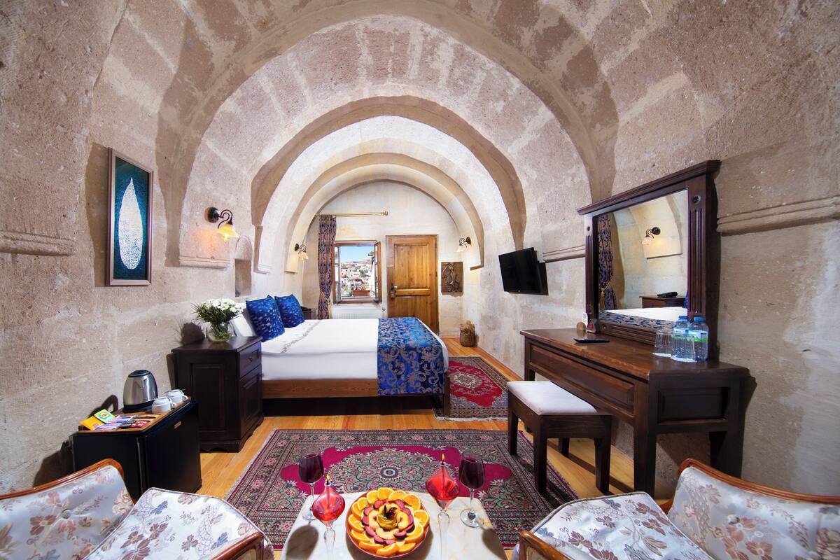 A room with a bed, a desk, a chair, a mirror, and a view through an arched doorway.