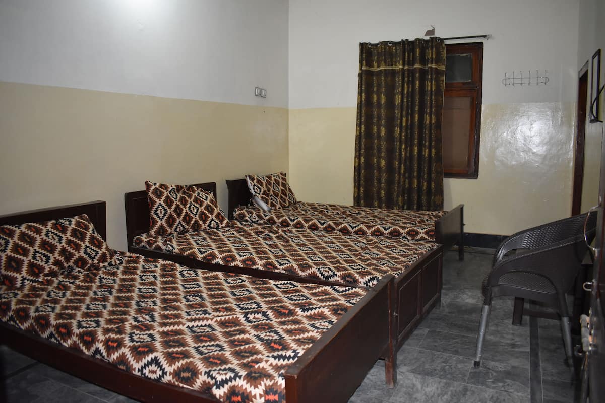 A room with two beds, a chair, a window with curtains, and a wall-mounted hook.