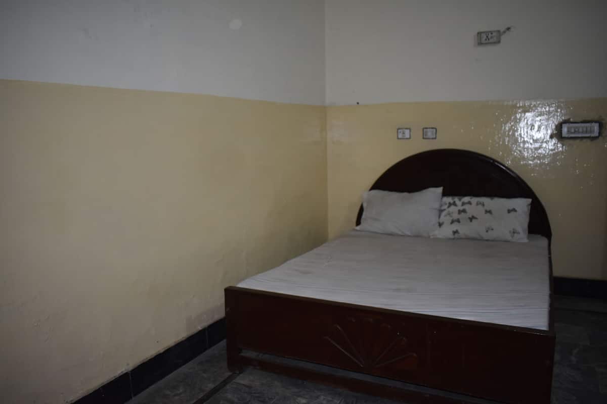 A single bed with a wooden headboard in a room with yellow walls and a tiled floor.
