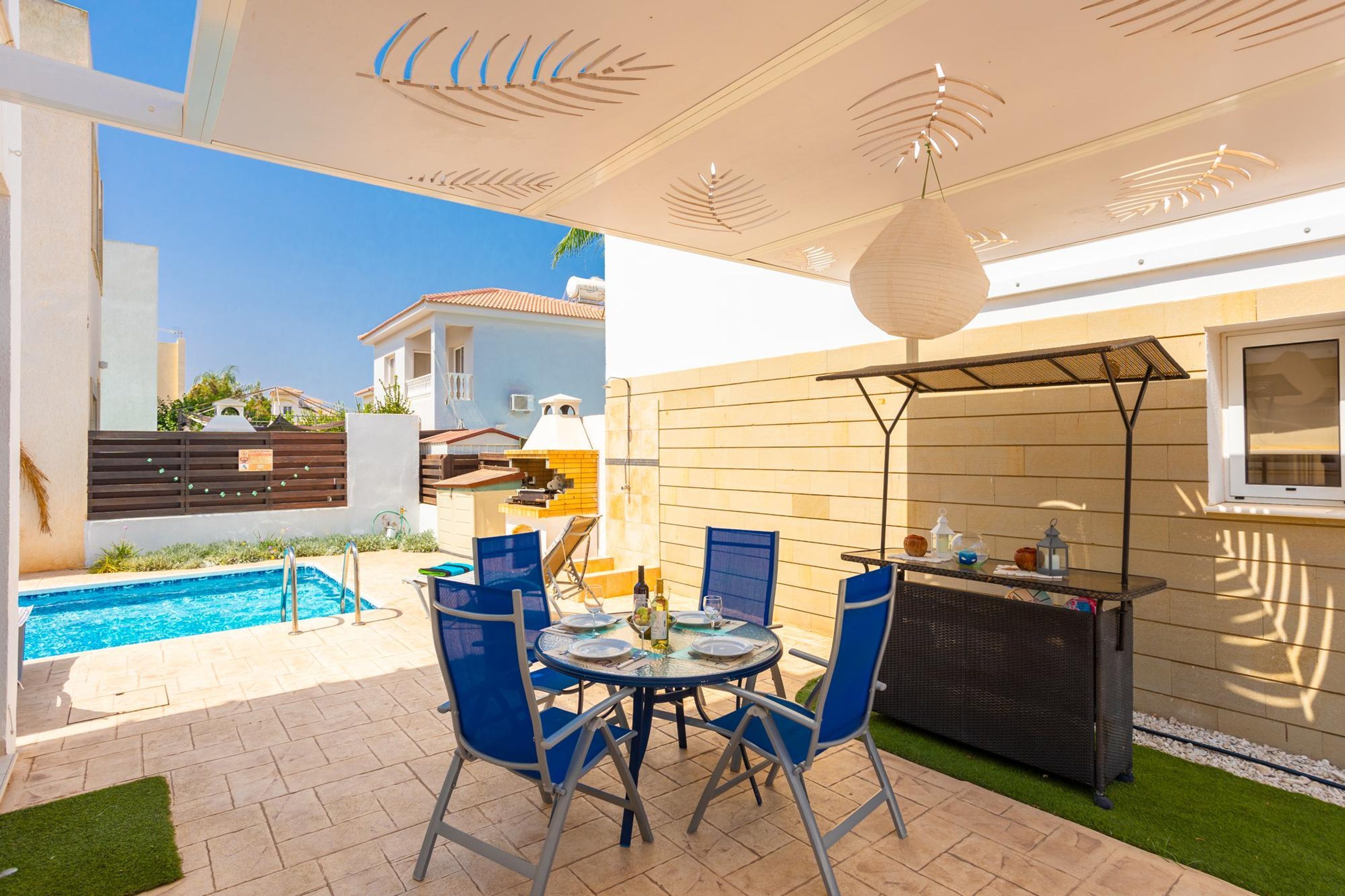 A patio area with a pool, a round table with chairs, and a bar.