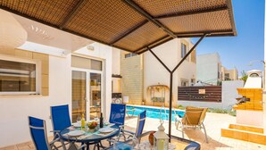 A poolside area with a glass table, blue chairs, and a covered seating area. - Villa Vitamin Blue in Pernera (Paralimni)