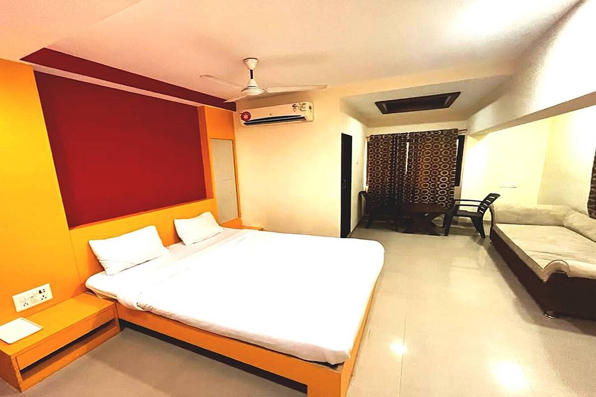 A bedroom with a single bed, a bedside table, a ceiling fan, an air conditioning unit, and a sofa.