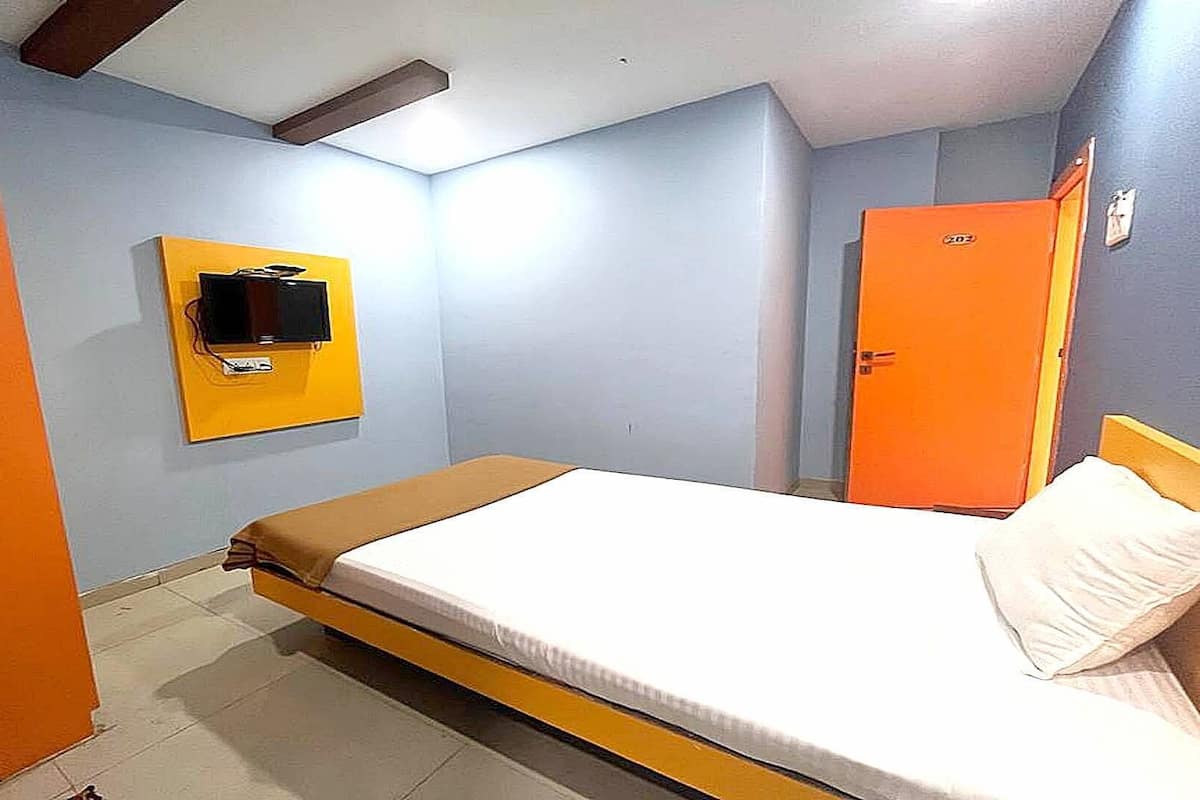 A single-bed room with a bed, a television mounted on the wall, and an orange door.