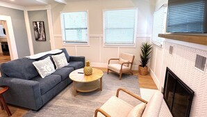 A living room with a grey sofa, a round coffee table, a beige armchair, and a fireplace. - Book & Stay Today + King Bed + Beach Chairs (Indian Rocks Beach)