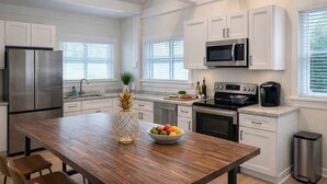 A modern kitchen with white cabinetry, stainless steel appliances, and a wooden dining table. - Book & Stay Today + King Bed + Beach Chairs (Indian Rocks Beach)