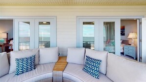 A covered outdoor seating area with two white sofas and patterned cushions, a wooden floor, and a ceiling fan.