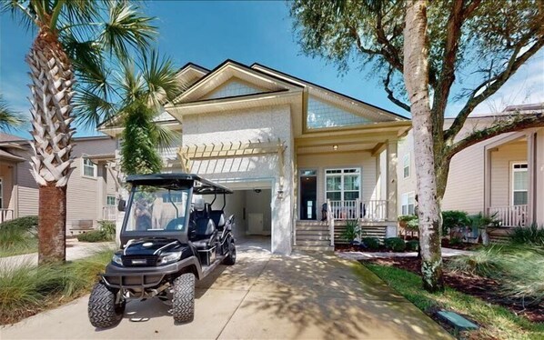 Two-story house with a garage entrance, surrounded by mature trees and well-maintained landscaping.