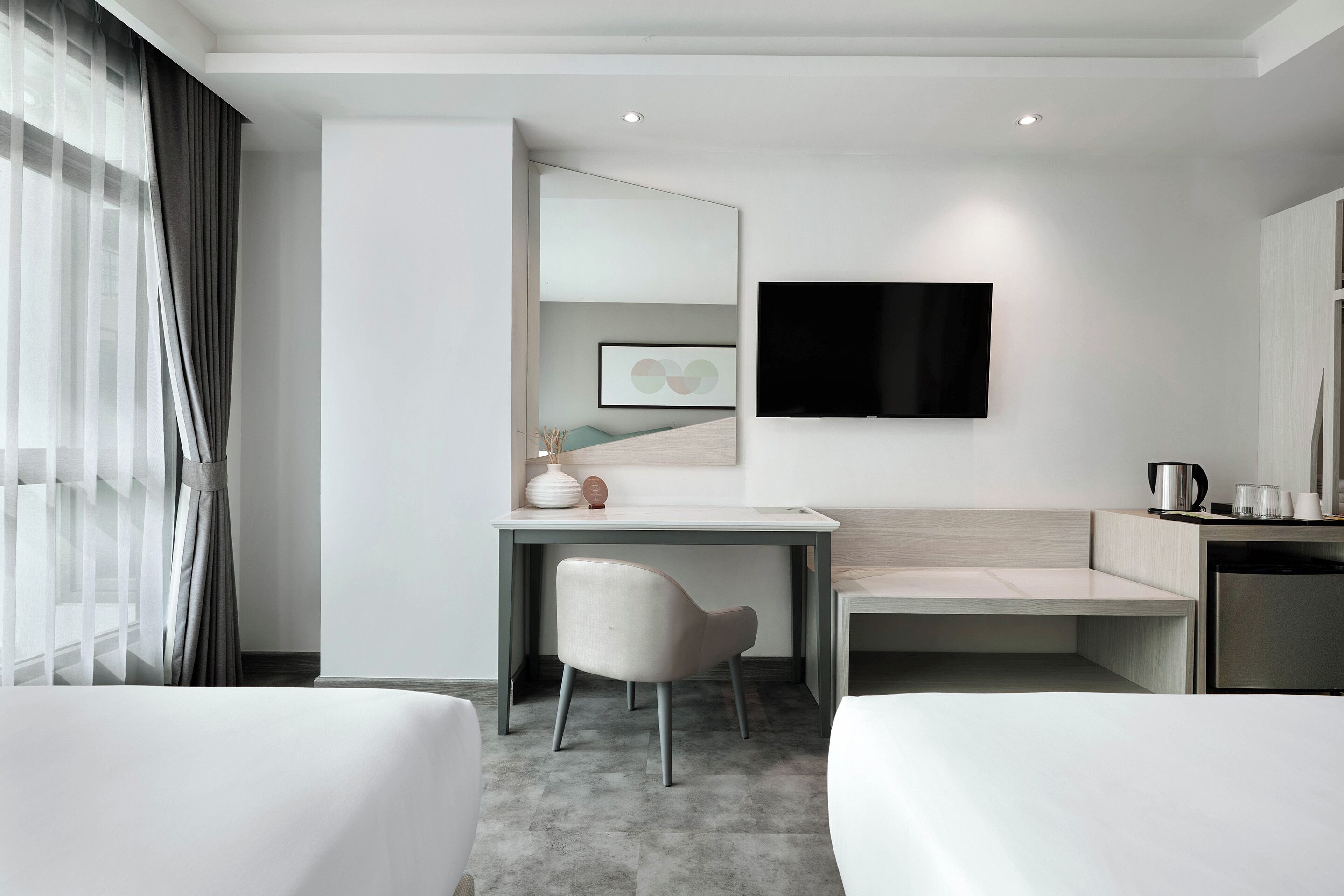 A modern hotel room with a bed, a desk, a chair, a TV, and a coffee machine.