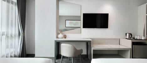 A modern hotel room with a bed, a desk, a chair, a TV, and a coffee machine.