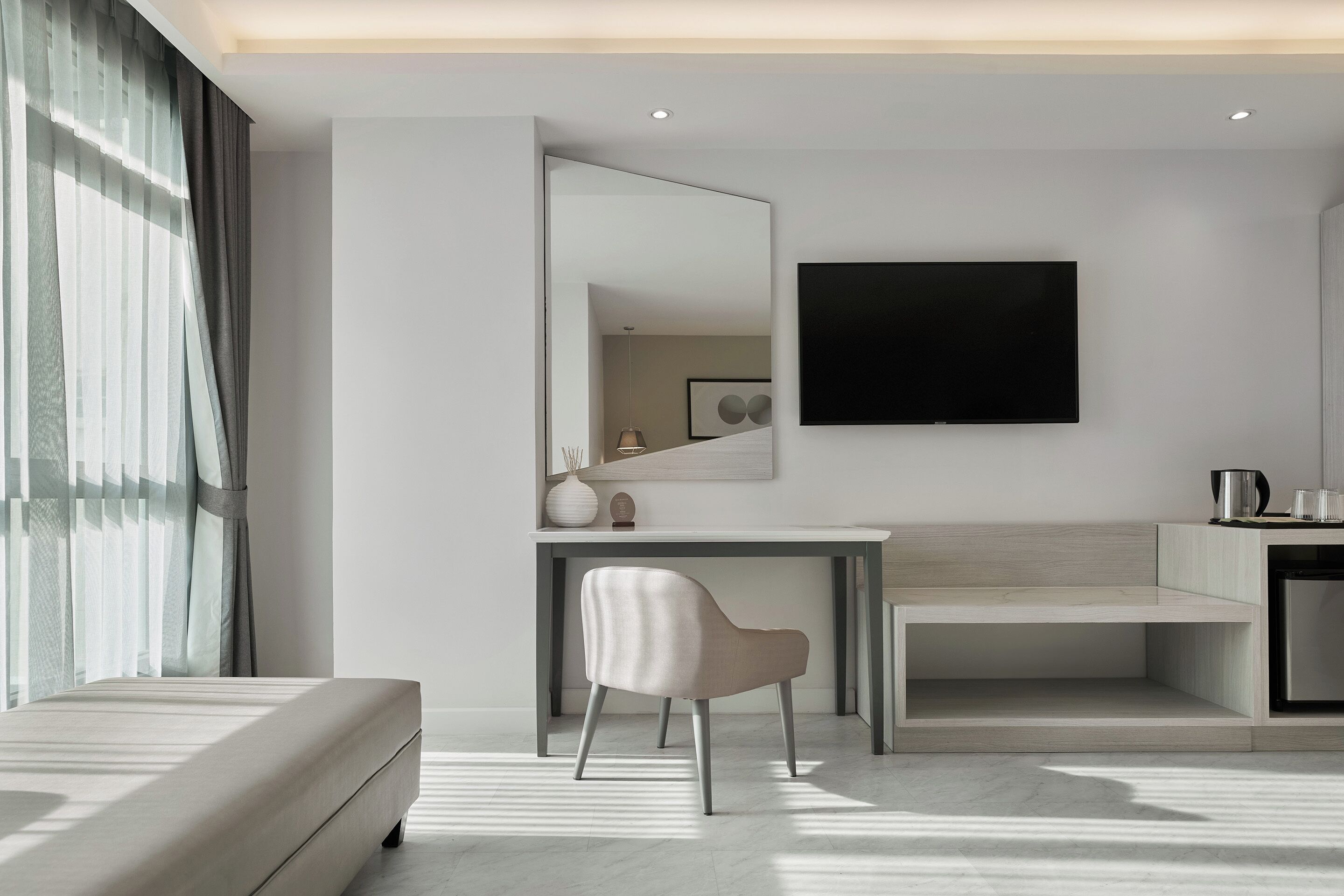 Una habitación de hotel moderna con una cama, un escritorio, una silla, un televisor de pantalla plana y un espejo grande.