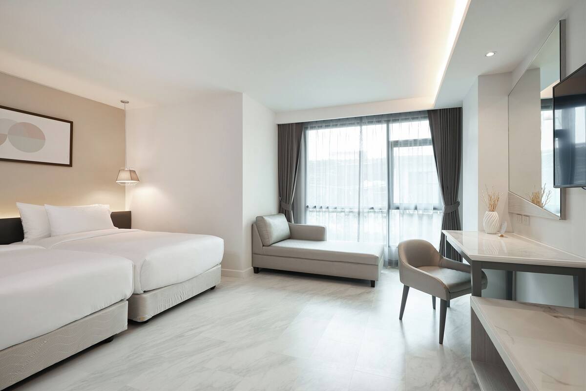 Una habitación de hotel moderna con dos camas, un sofá, un escritorio y un ventanal con cortinas.