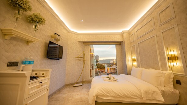 A hotel room with a bed, a TV, a wardrobe, and a window with a city view. - ACJ Residence - A Member of The Luxury Stay Group (Kota Kinabalu)