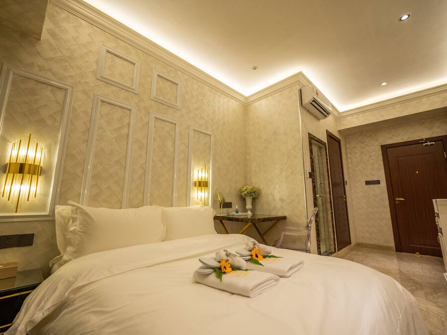 A hotel room with a large bed, a bedside table with a lamp, and a door leading to another room.