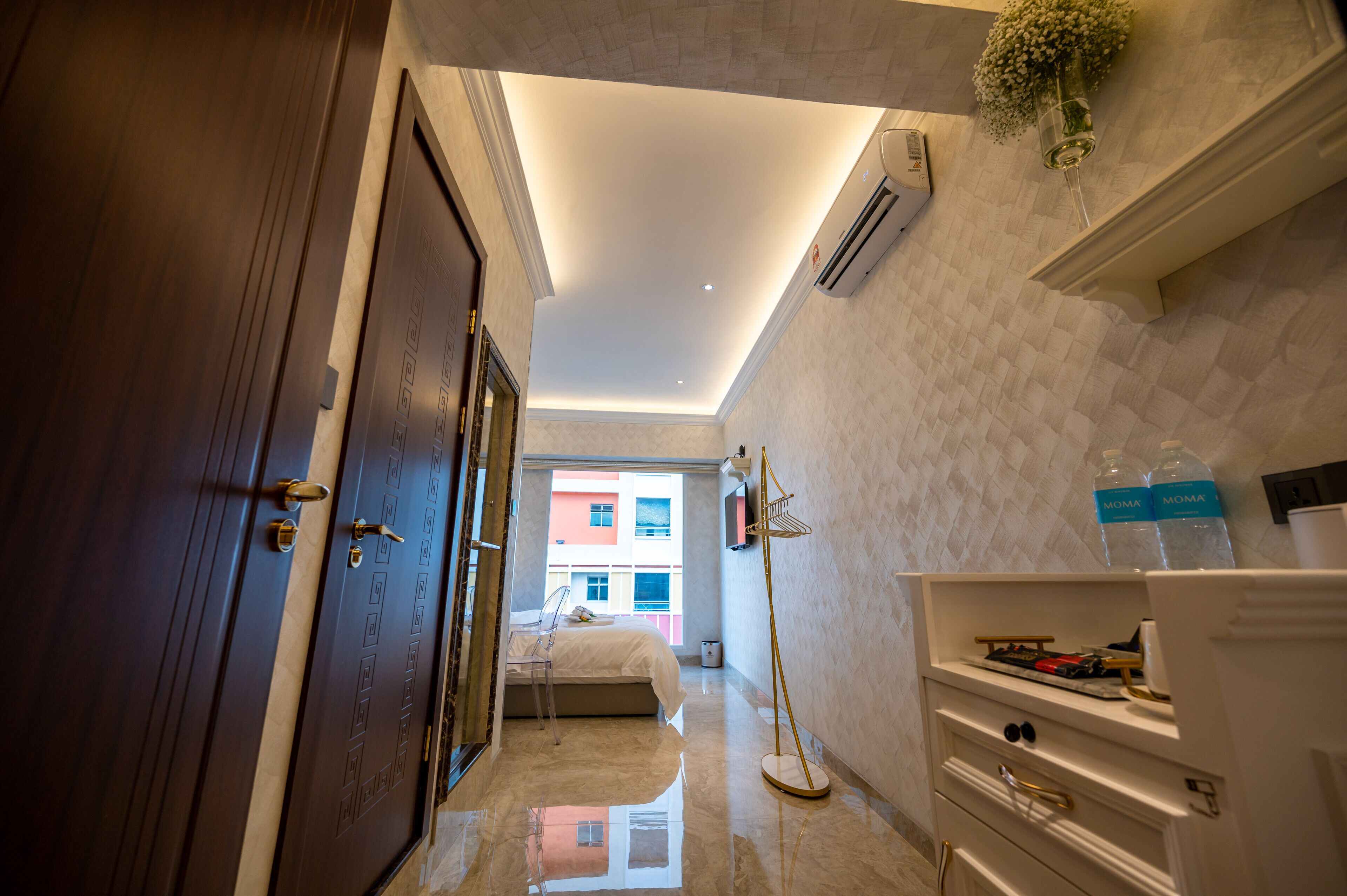 A hotel room with a bed, a desk, a mirror, a wardrobe, and an air conditioning unit.