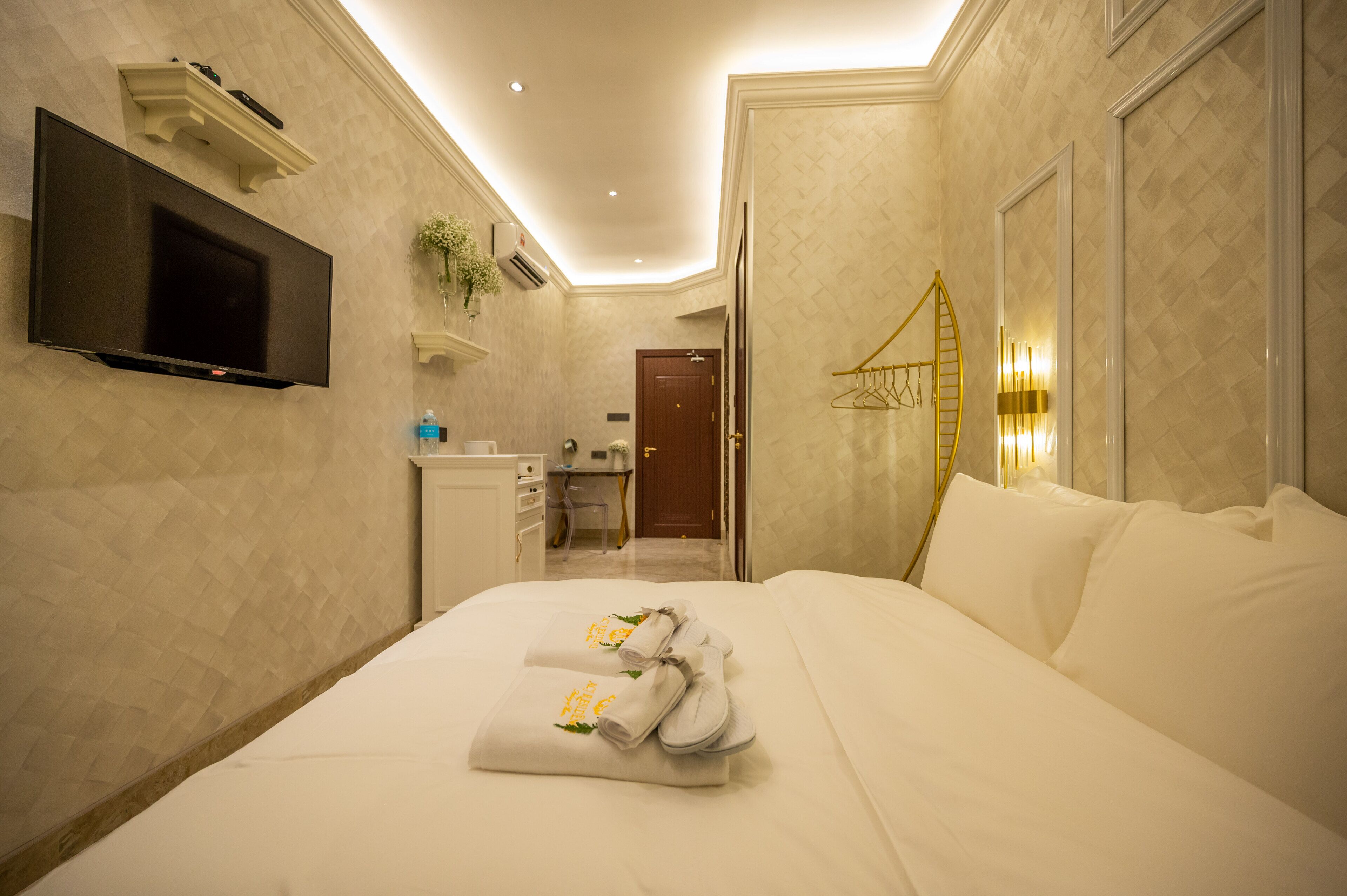 A hotel room with a bed, a TV mounted on the wall, a desk with a chair, a bathroom, and a door.