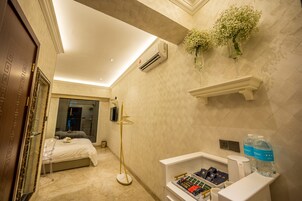 Habitación de hotel con cama, lámpara de pie, tocador con artículos de aseo y aire acondicionado de pared.