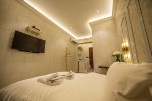 A hotel room with a bed, a flat-screen TV mounted on the wall, a bedside table with a vase of flowers, and a wall-mounted air conditioning unit. - ACJ Residence - A Member of The Luxury Stay Group (Kota Kinabalu)