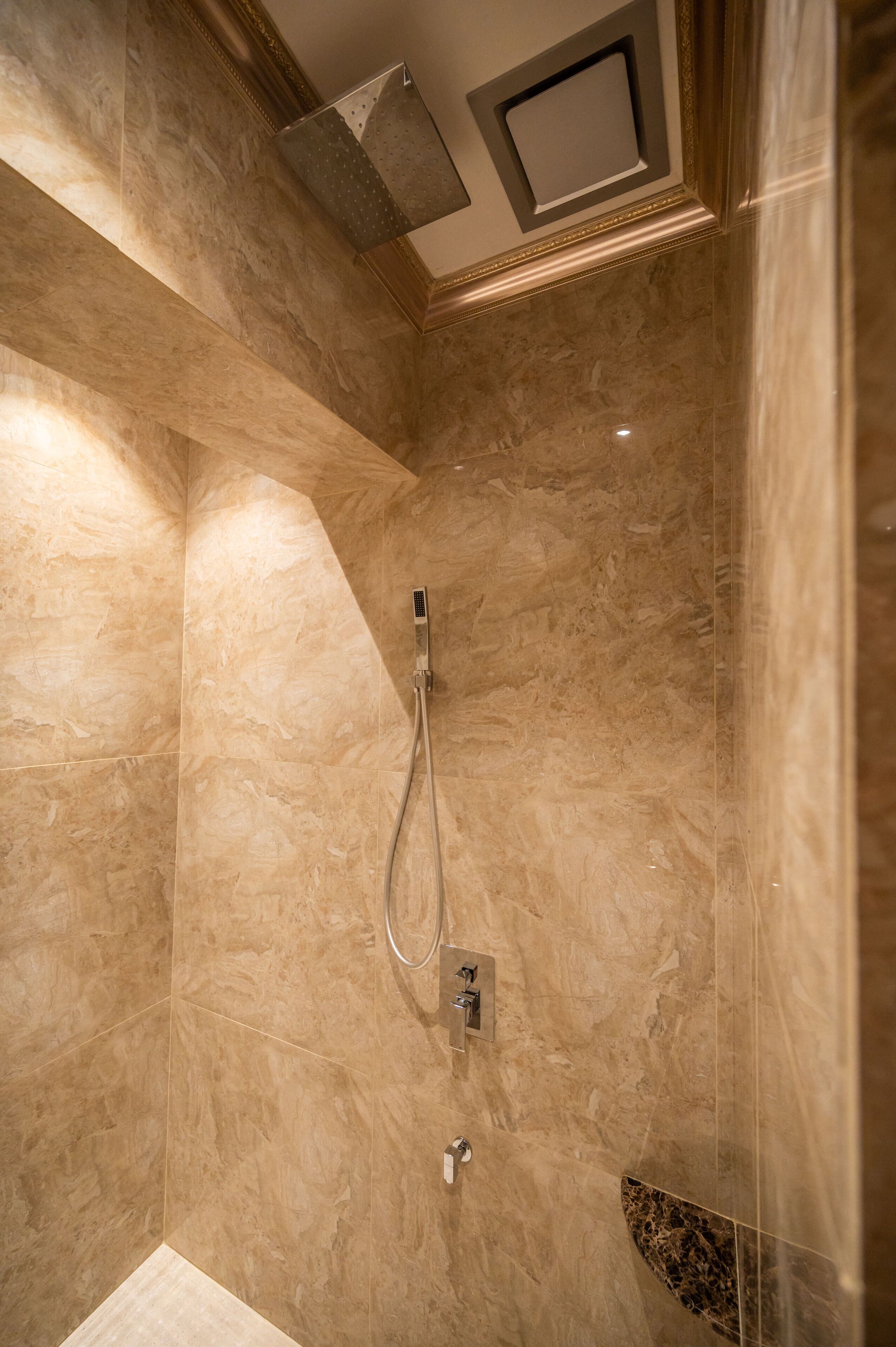 A modern bathroom with marble walls, a shower with a handheld showerhead, and a built-in light fixture.