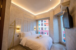 A hotel room with a bed, a TV mounted on the wall, and a window with a view of colorful buildings. - ACJ Residence - A Member of The Luxury Stay Group (Kota Kinabalu)