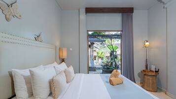 A spacious bedroom with a large bed, a view of the outdoor garden, and a wooden ceiling beam.