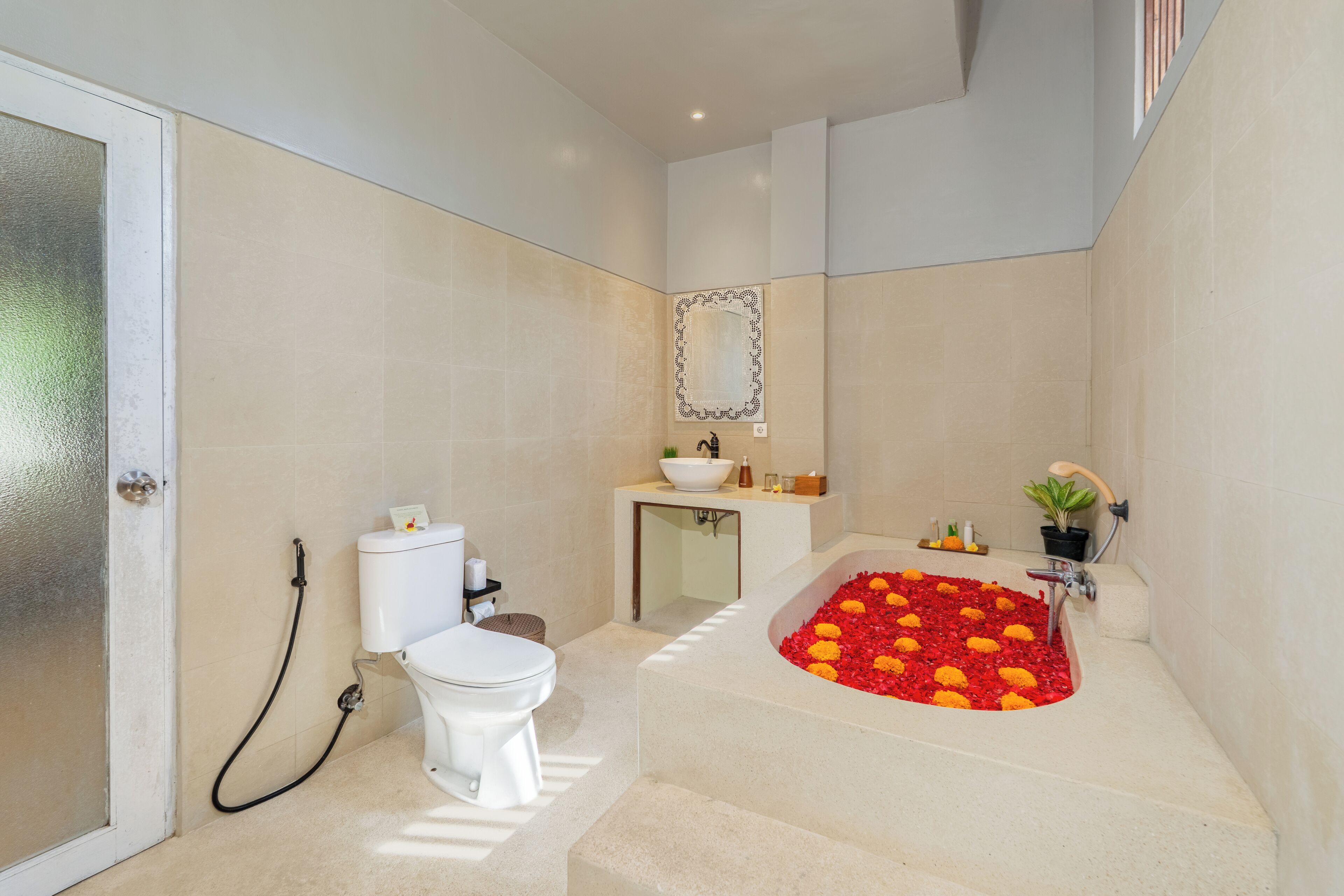 A modern bathroom with a toilet, sink, and a large bathtub filled with flowers.