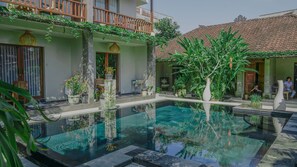 A courtyard with a swimming pool, potted plants, and a traditional tiled roof. - Lokasari Retreat (Ubud)