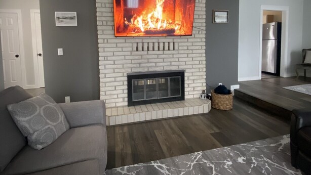 Una sala de estar con chimenea, un sofá y un televisor montado en una pared de ladrillo.