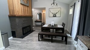 Un comedor espacioso con una mesa y bancos de madera, una chimenea y una cocina moderna con baldosas oscuras.