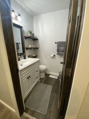 A bathroom with a white sink, dark wooden floor, a white toilet, and a towel hanging on the wall.