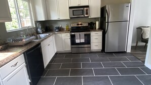 Una cocina moderna con armarios blancos, electrodomésticos de acero inoxidable y piso de baldosas.