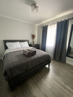 A bedroom with a bed, a nightstand, a vase, and a window with curtains.