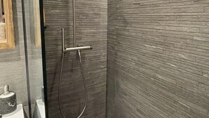 A modern shower with a rain showerhead and handheld showerhead, tiled walls, and a glass door.