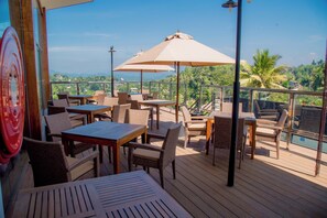 A terrace with wicker furniture, a table, and an umbrella, overlooking a scenic landscape with hills and palm trees. - Lavendish Hills Kandy (Kandy)