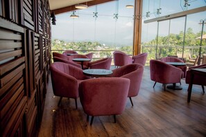 A restaurant with wooden flooring, red chairs, and tables, featuring a view of a cityscape through large windows. - Lavendish Hills Kandy (Kandy)