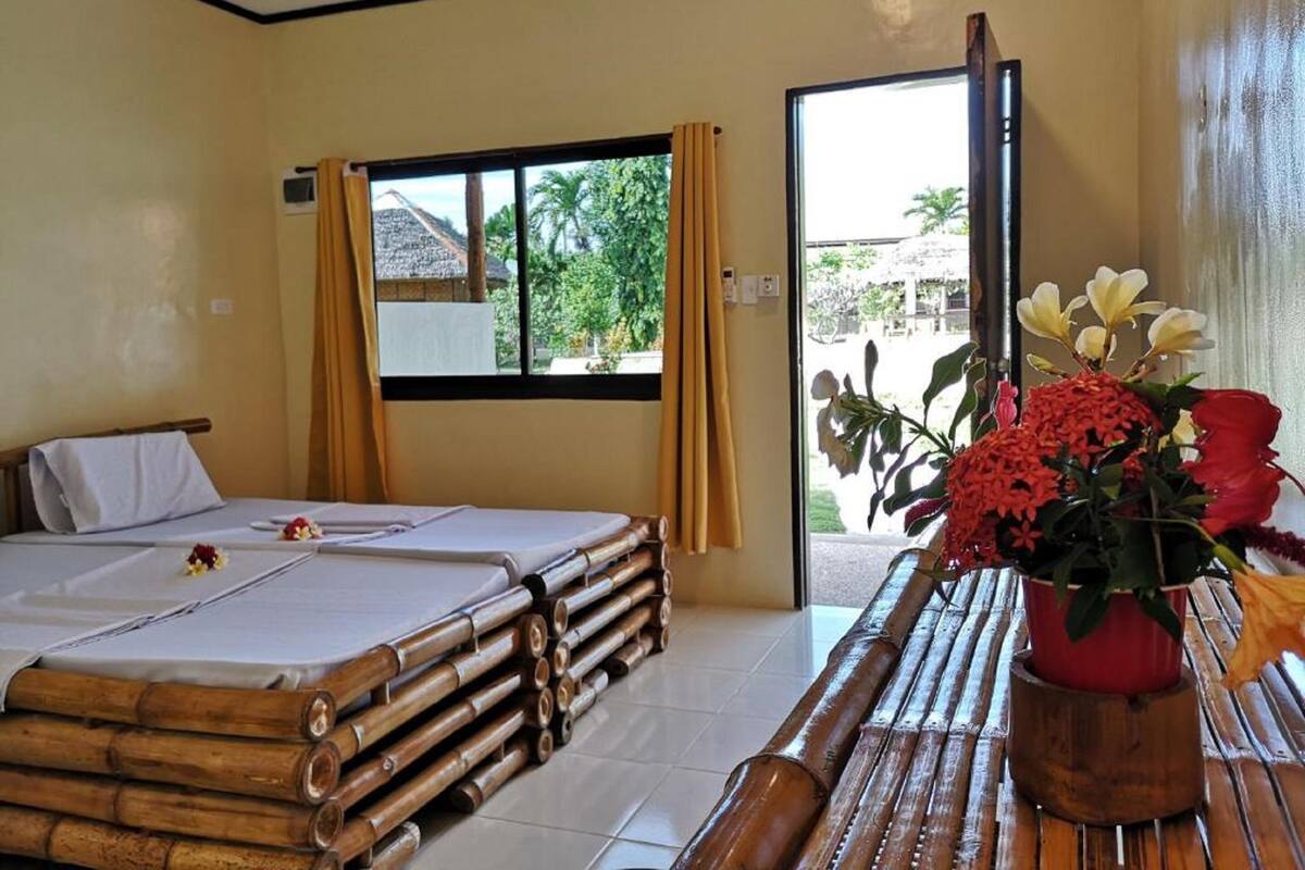A room with a bed, a window, a ceiling fan, and a table with a potted plant.