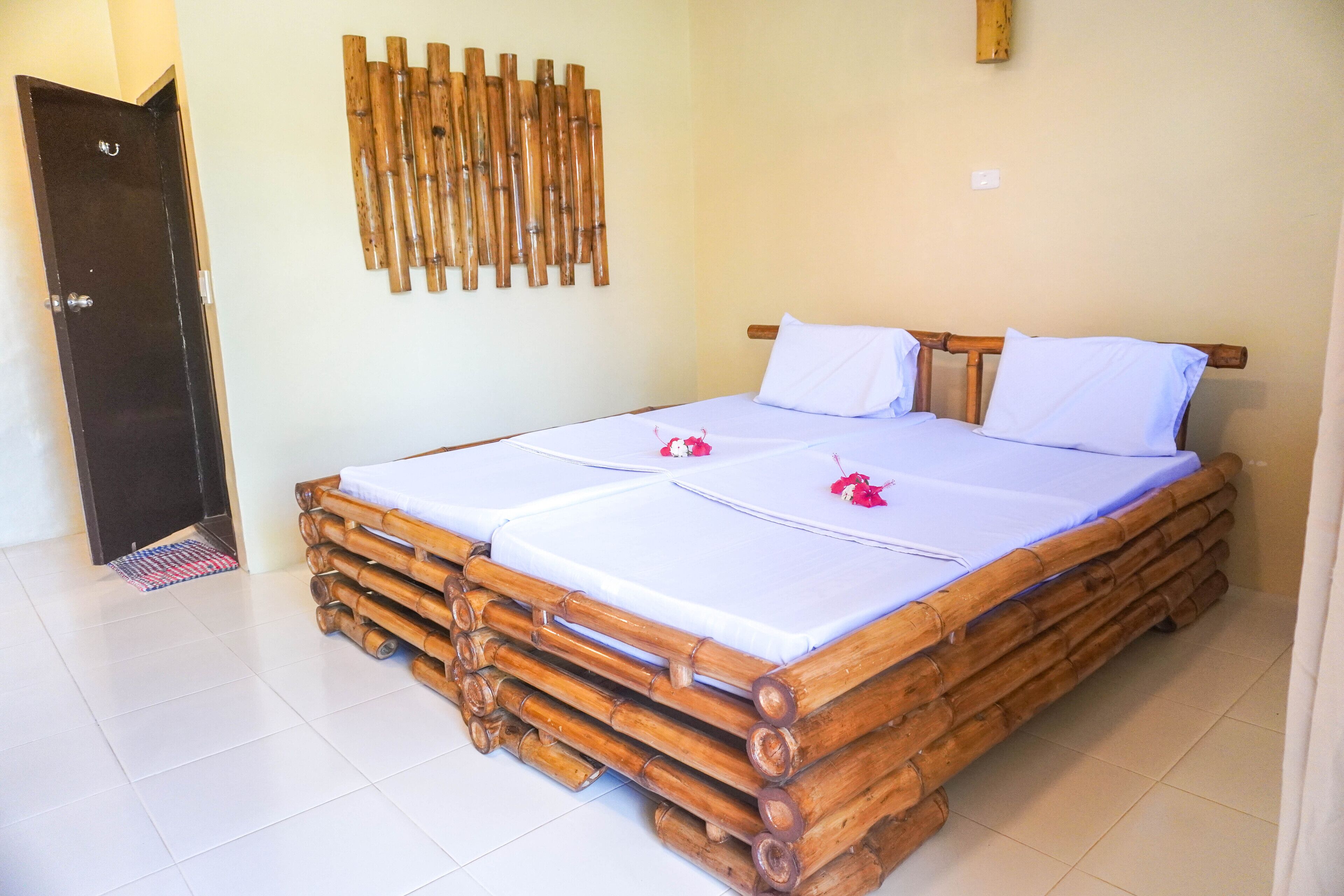 A room with a bamboo bed frame, two white bedsheets, and a decorative bamboo wall panel.