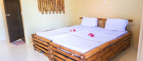 A room with a bamboo bed frame, two white bedsheets, and a decorative bamboo wall panel.