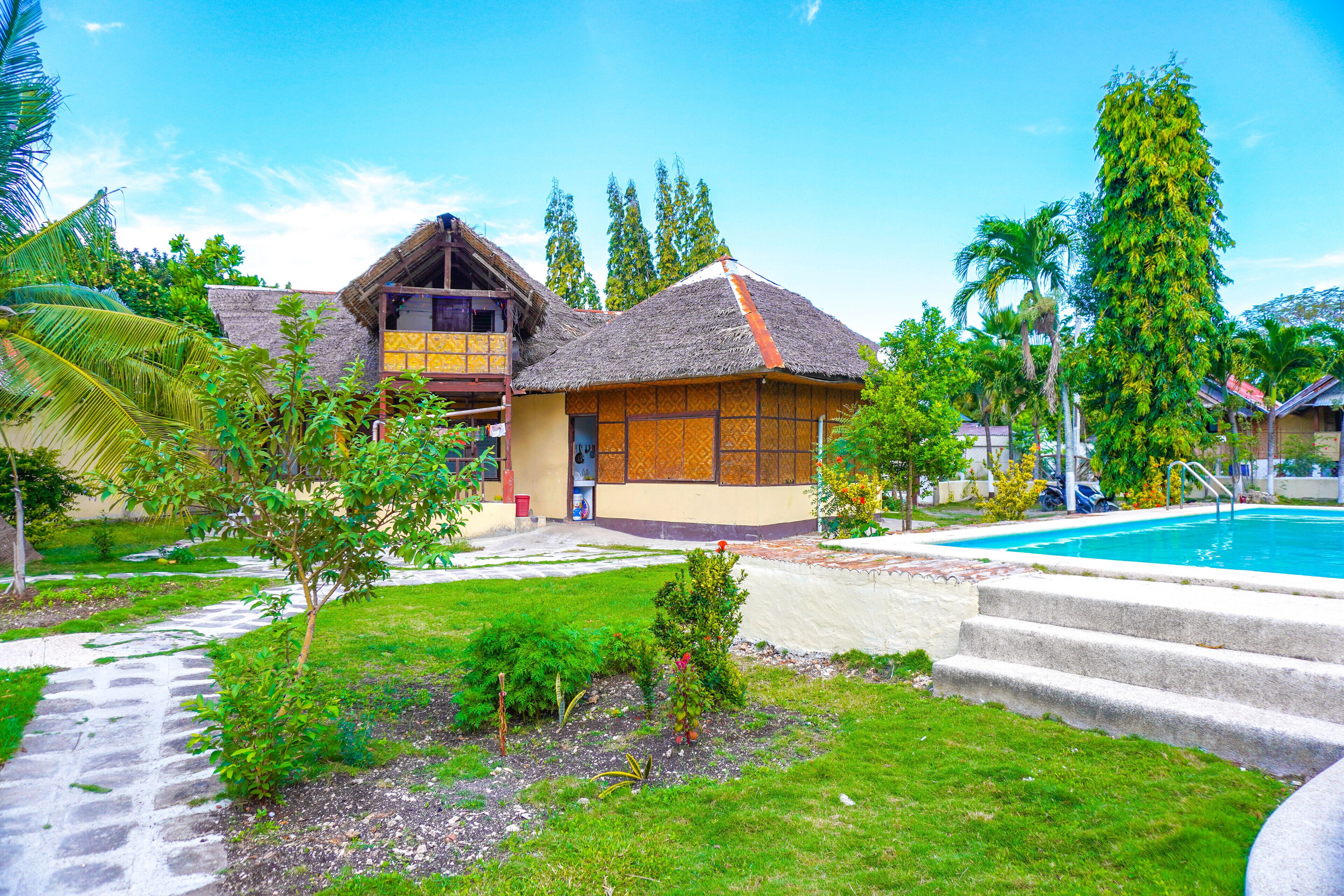 Une maison traditionnelle avec un toit de chaume, entourée d’une végétation luxuriante et dotée d’une piscine.