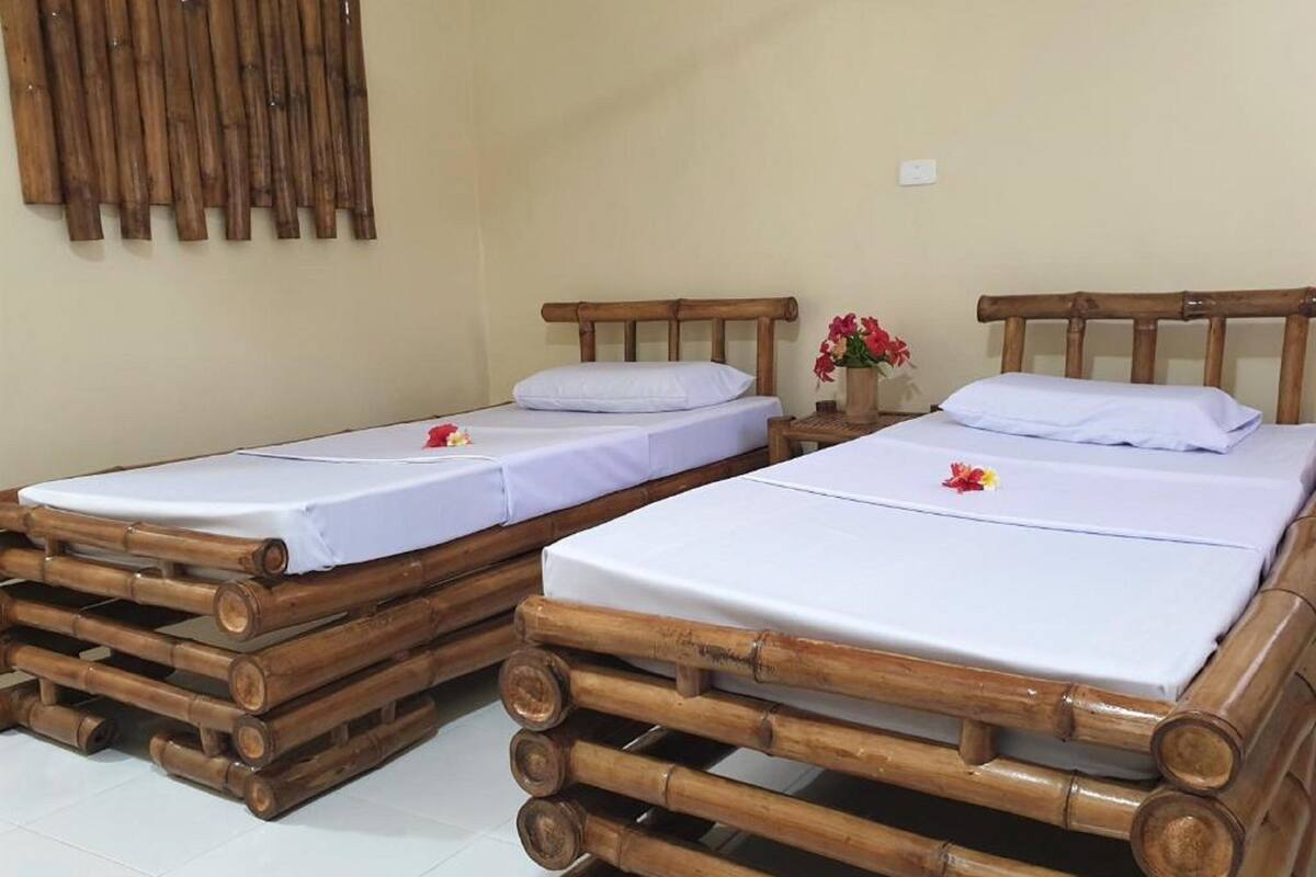 Two single beds with wooden frames and white linens, arranged in a room with tiled flooring.