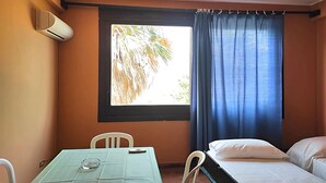 Una habitación con cama, una mesa con silla, una ventana con cortinas e un equipo de aire acondicionado.