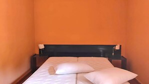 Habitación de hotel con una pared naranja, un cabecero negro y una cama con ropa de cama blanca.