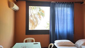 A room with a single bed, a small table, a chair, and a window with curtains. - Belvilla by OYO Appealing apartment with pool (Sant'Irene-torre Vecchia)