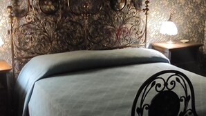 Una cama con estructura metálica y cabecera con diseños elaborados. Hay dos mesitas de noche con lámparas.