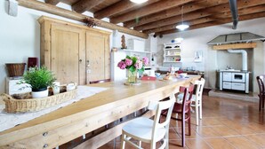 A rustic kitchen with wooden beams, a long wooden table, and white chairs. - Holiday Home in Feltre with Garden BBQ (Pedavena)