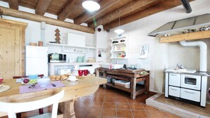 A rustic kitchen with wooden beams, a wooden table, and white appliances. - Holiday Home in Feltre with Garden BBQ (Pedavena)