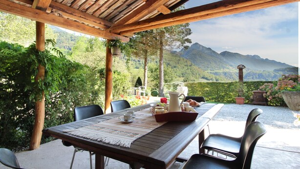 An outdoor dining area with a wooden pergola, a table set with tableware, and a scenic mountain view. - Holiday Home in Feltre with Garden BBQ (Pedavena)